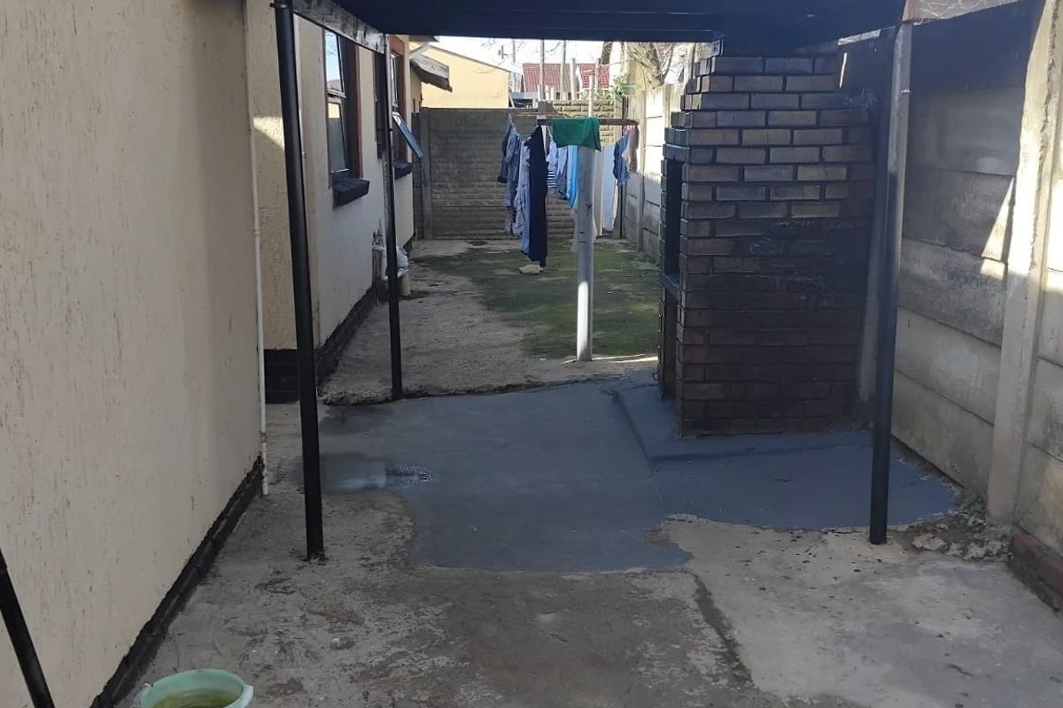 Rear exterior area featuring a built-in brick braai, covered patio space, and concrete flooring, enclosed by precast boundary walls.