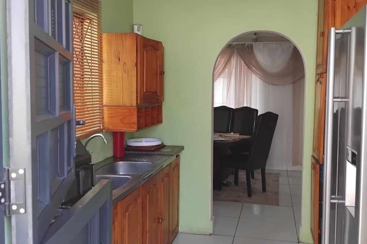 A functional kitchen featuring wooden cabinetry, a double stainless steel sink, and an arched doorway leading to the dining area.