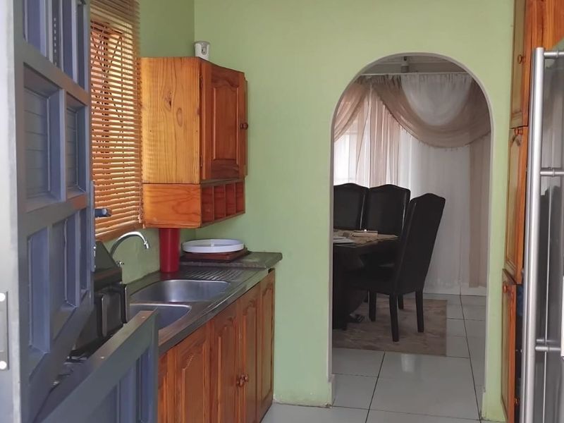 A functional kitchen featuring wooden cabinetry, a double stainless steel sink, and an arched doorway leading to the dining area.