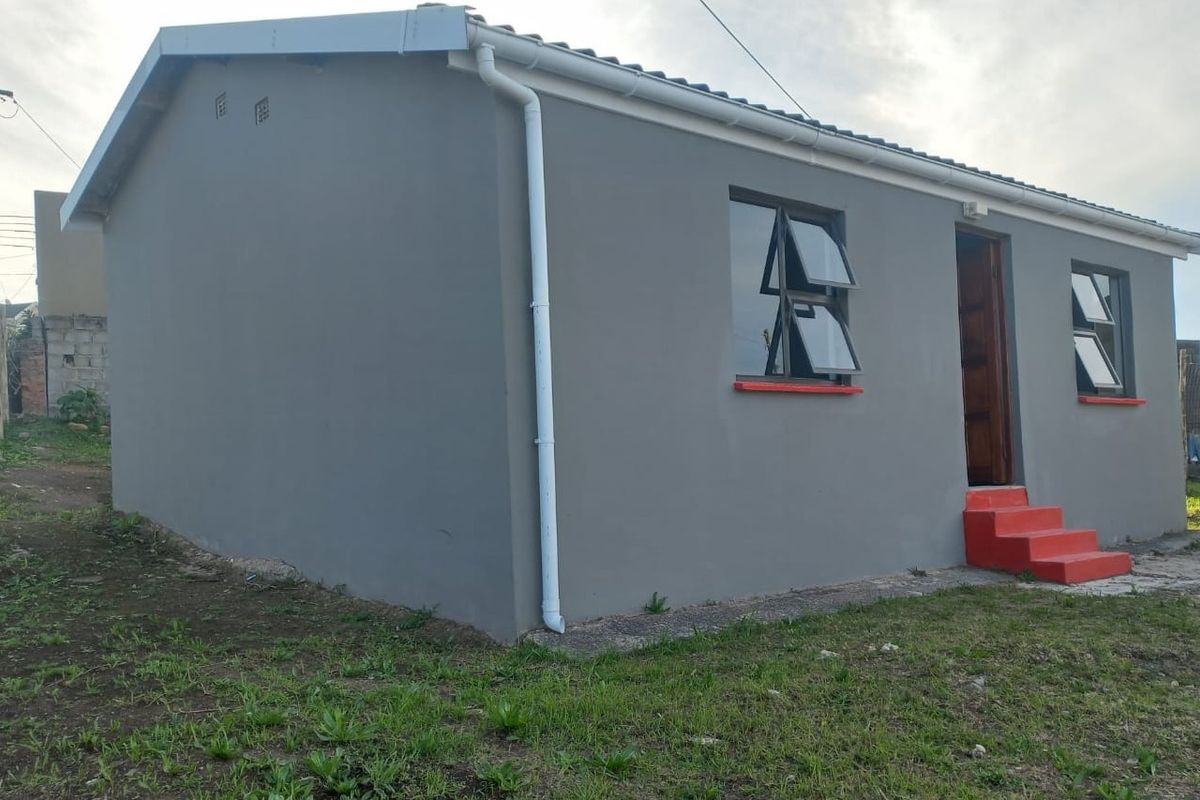 A side view of a single-story residential house featuring grey painted exterior walls, top-hung windows, and concrete entrance steps.