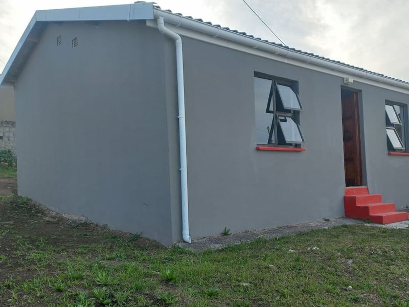 A side view of a single-story residential house featuring grey painted exterior walls, top-hung windows, and concrete entrance steps.