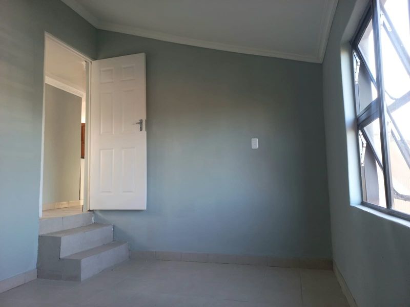 An empty bedroom featuring tiled flooring, neutral wall paint, and a stepped transition leading to an adjacent room.