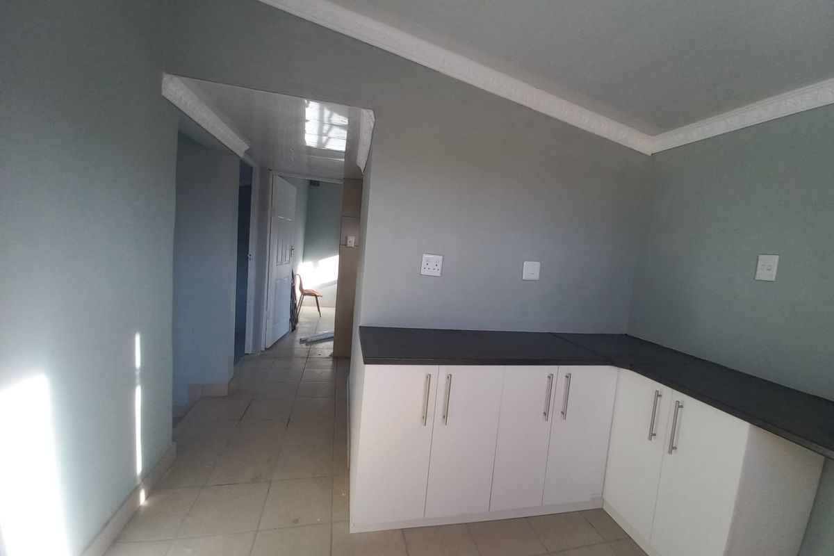 A functional kitchen area featuring white built-in cabinetry with dark countertops and tiled flooring, leading into a hallway.