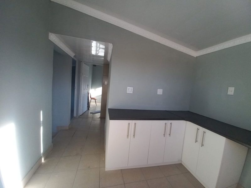 A functional kitchen area featuring white built-in cabinetry with dark countertops and tiled flooring, leading into a hallway.
