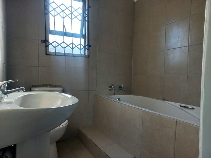 A functional bathroom featuring a pedestal basin, built-in bathtub, and neutral wall tiling, complete with a security-fitted window.