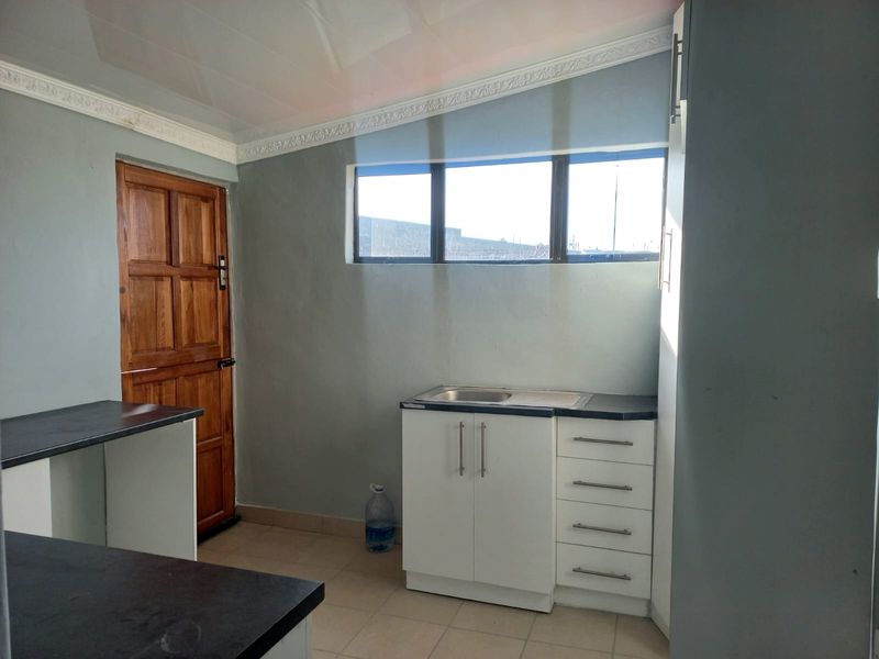 A functional scullery or utility area featuring built-in white cabinetry, a stainless steel sink, dark laminate countertops, and tiled flooring.