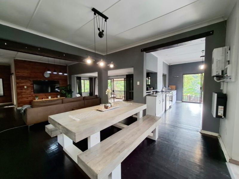 Spacious open-plan living, dining, and kitchen area featuring dark timber flooring, exposed ceiling beams, and direct access to an outdoor patio.