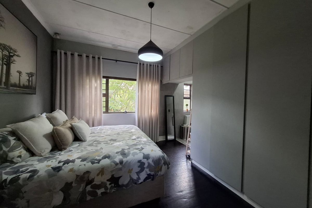 A well-maintained bedroom featuring dark timber flooring, extensive built-in cabinetry, and a central pendant light fixture.