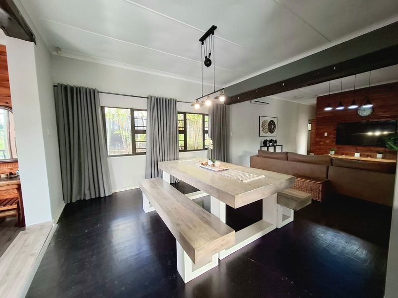 Spacious open-plan living and dining area featuring dark timber flooring, exposed ceiling beams, and warm timber wall accents, creating a comfortable and inviting atmosphere.