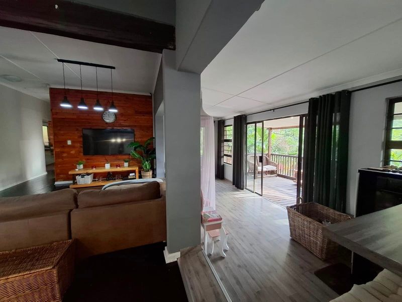 Open plan living area featuring a timber accent wall, laminate flooring, and large sliding doors providing seamless access to the outdoor deck.