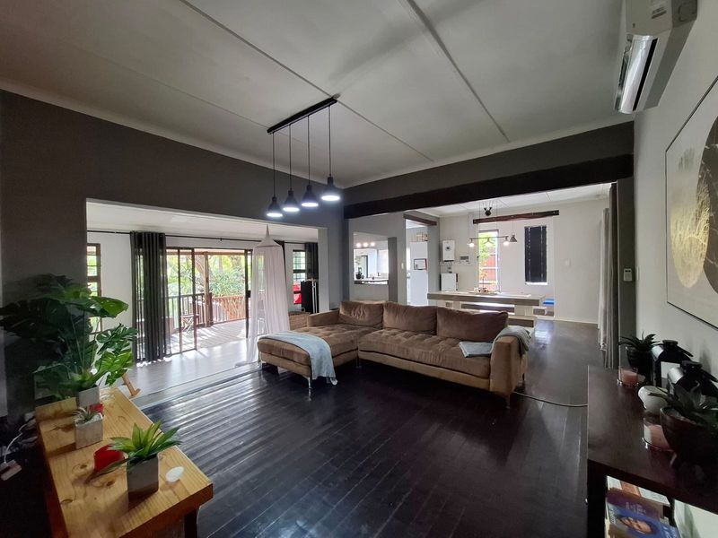 Spacious open-plan living area featuring dark timber flooring, modern pendant lighting, and seamless flow to an outdoor patio space.
