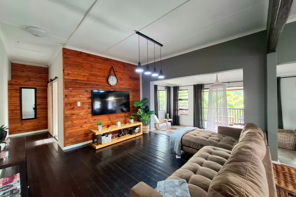 Spacious living room featuring warm timber wall cladding, dark stained wooden floors, and modern pendant lighting, with an open flow to the adjacent patio area.
