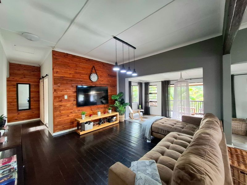 Spacious living room featuring warm timber wall cladding, dark stained wooden floors, and modern pendant lighting, with an open flow to the adjacent patio area.