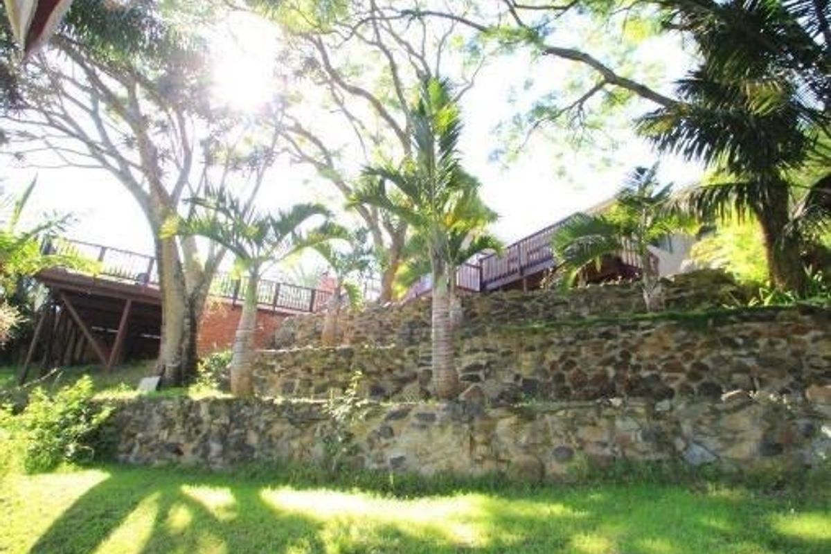 Rear garden view featuring tiered stone retaining walls and a raised timber deck with balustrade, set within a mature landscaped environment.