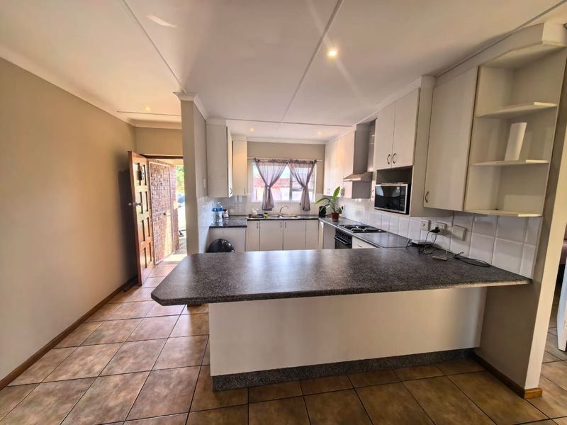 A functional kitchen featuring white cabinetry, dark laminate countertops, a breakfast bar, and tiled flooring, with direct access to the entrance area.