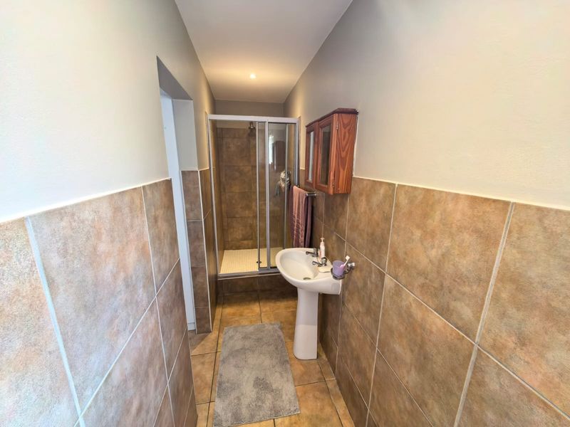 A functional bathroom featuring a pedestal basin, a tiled shower enclosure, and neutral wall tiling throughout.