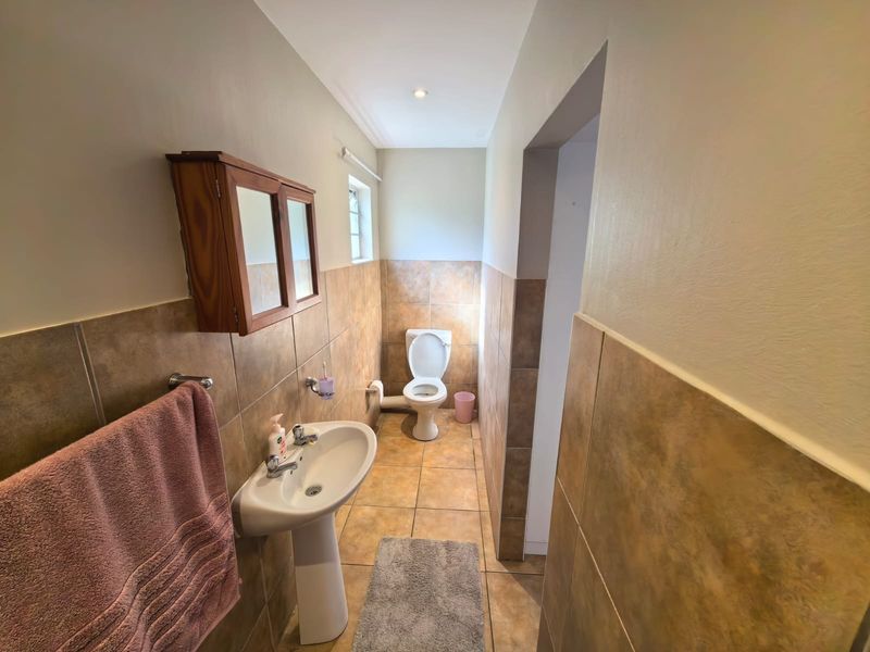 A functional bathroom featuring a pedestal basin, toilet, and wall-mounted medicine cabinet with neutral tiled finishes.