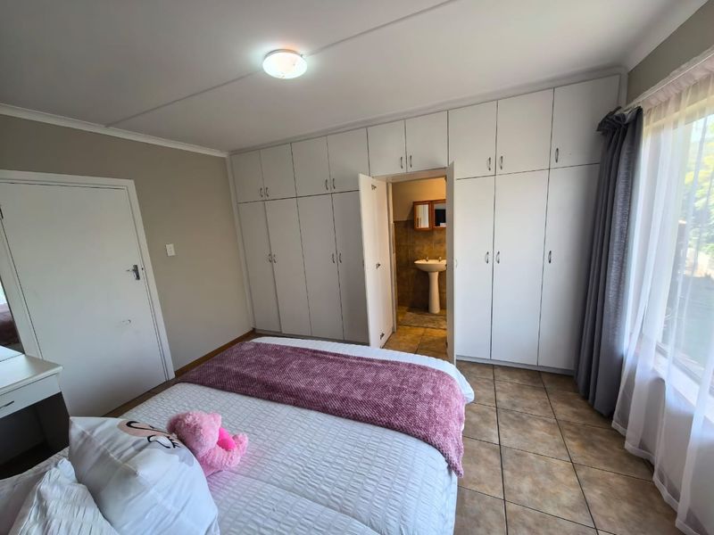 A bedroom featuring extensive built-in cupboards, tiled flooring, and direct access to an en-suite bathroom.