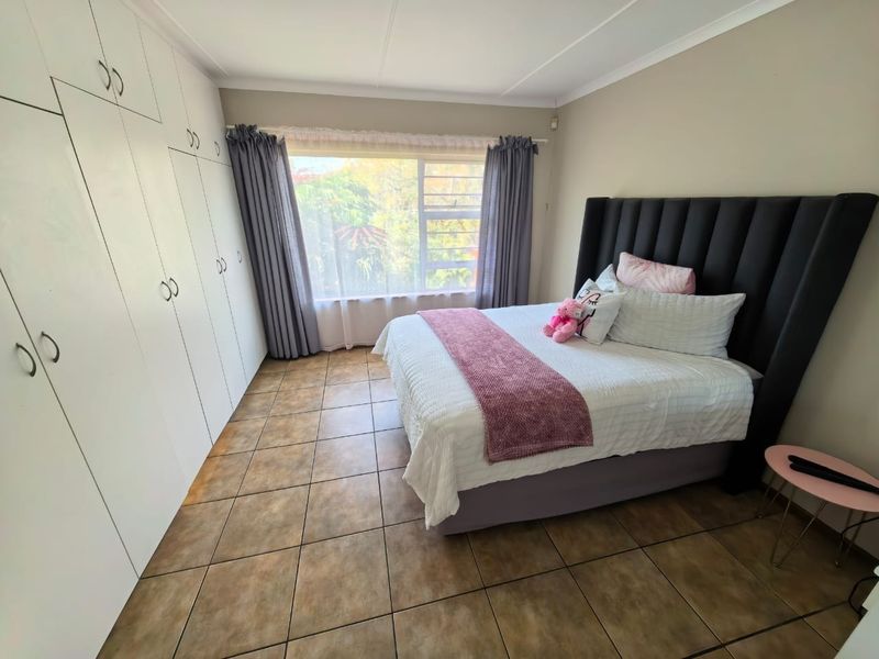 A well-lit bedroom featuring tiled flooring, ample built-in cupboard storage, and a large window providing natural light.