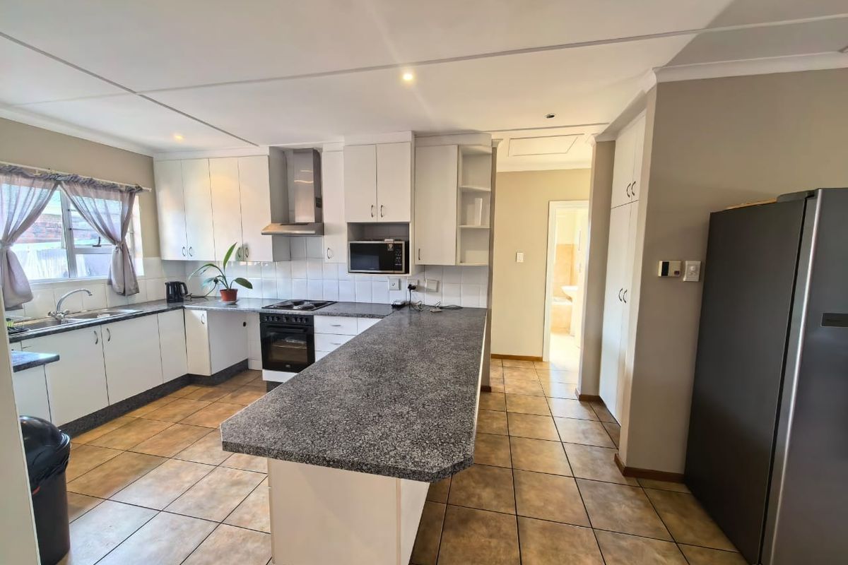 Functional kitchen featuring white cabinetry, granite countertops, built-in oven with extractor fan, and tiled flooring, offering a practical layout with ample storage space.