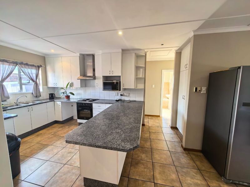 Functional kitchen featuring white cabinetry, granite countertops, built-in oven with extractor fan, and tiled flooring, offering a practical layout with ample storage space.