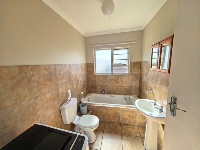 A functional bathroom featuring a built-in bathtub, pedestal basin, toilet, and tiled finishes, offering a neutral space ready for potential cosmetic updates.