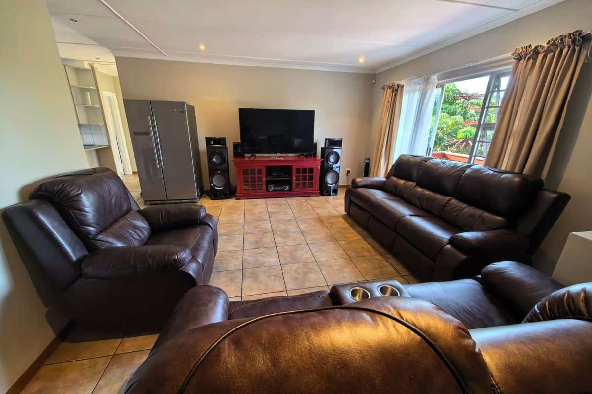 Spacious living room featuring tiled flooring, recessed downlighting, and large windows allowing natural light, with an open transition to the adjacent kitchen area.