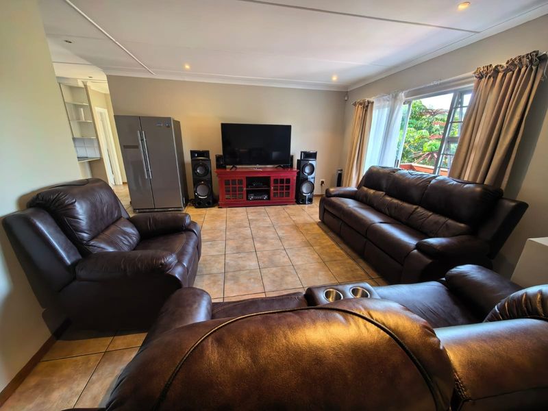 Spacious living room featuring tiled flooring, recessed downlighting, and large windows allowing natural light, with an open transition to the adjacent kitchen area.