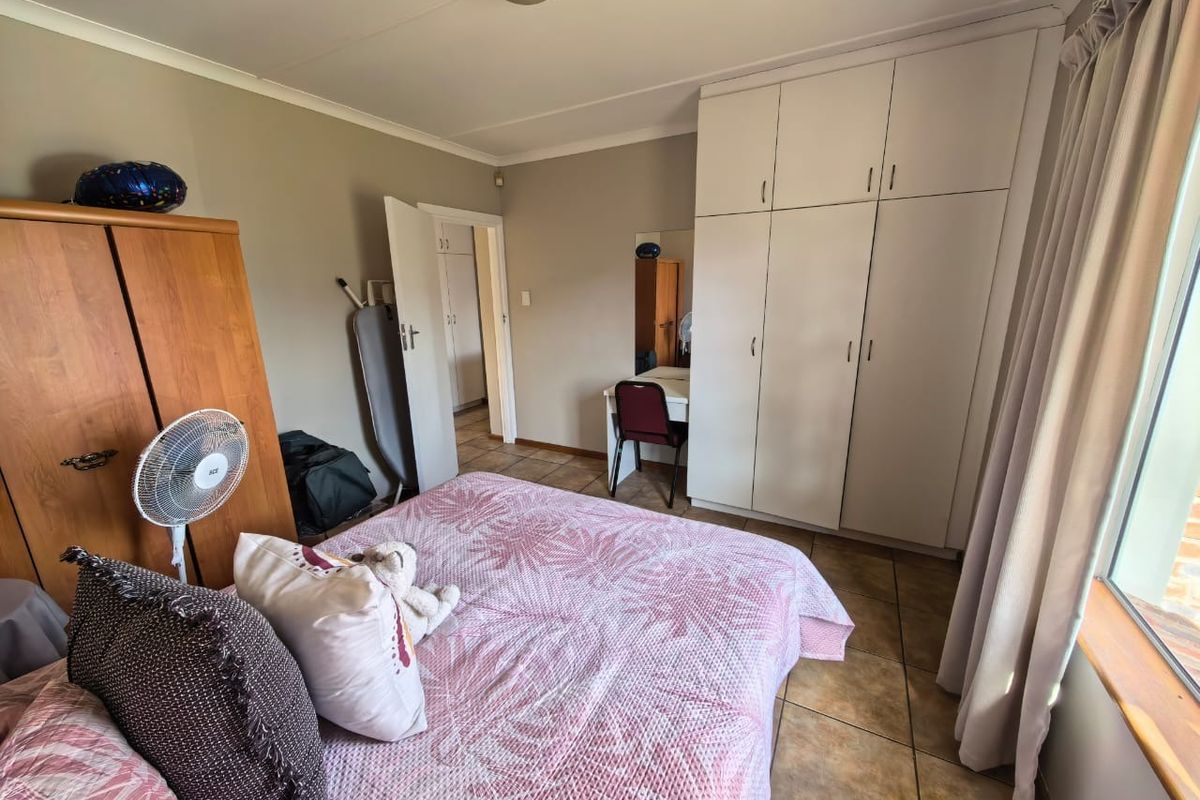 A bedroom featuring tiled flooring and built-in cupboards, offering a functional layout with natural light from the adjacent window.
