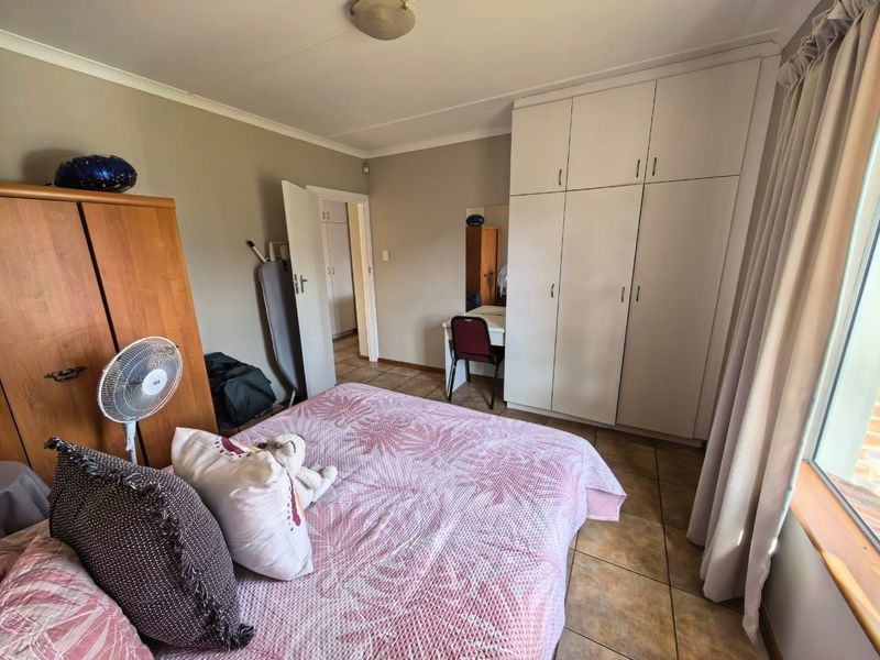 A bedroom featuring tiled flooring and built-in cupboards, offering a functional layout with natural light from the adjacent window.
