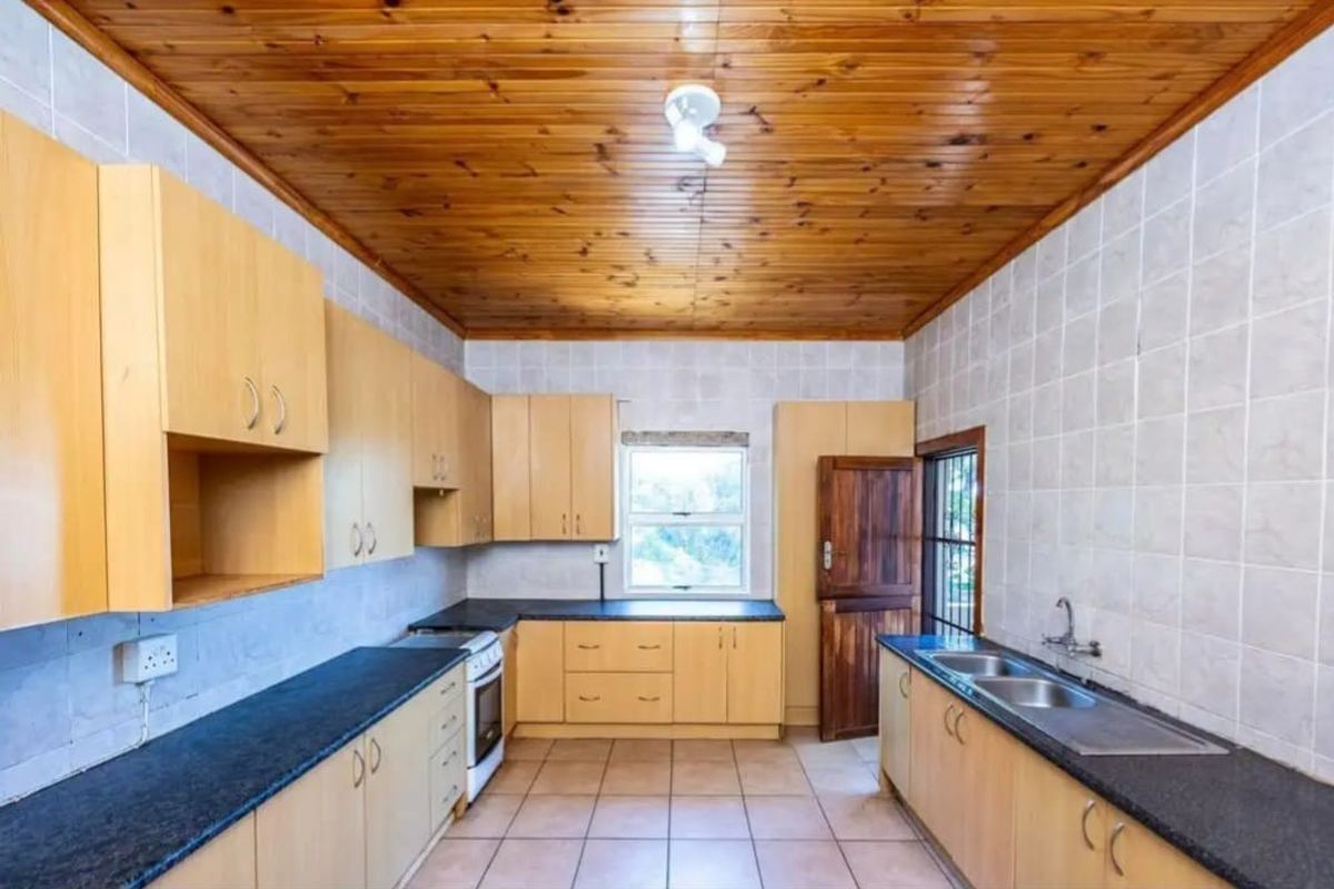 A functional kitchen featuring light wood cabinetry, dark stone countertops, a double sink, and a distinctive timber-clad ceiling.