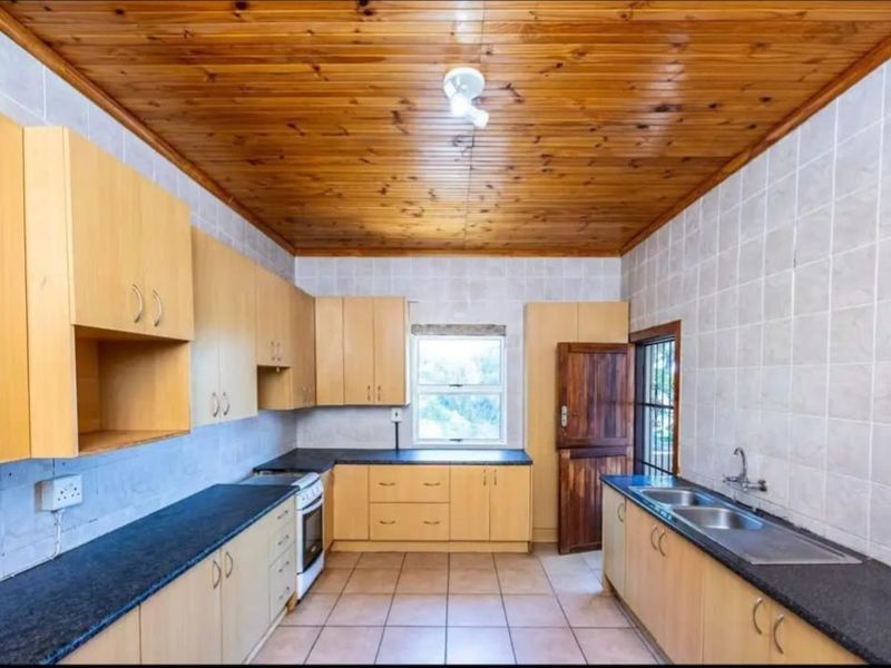 A functional kitchen featuring light wood cabinetry, dark stone countertops, a double sink, and a distinctive timber-clad ceiling.