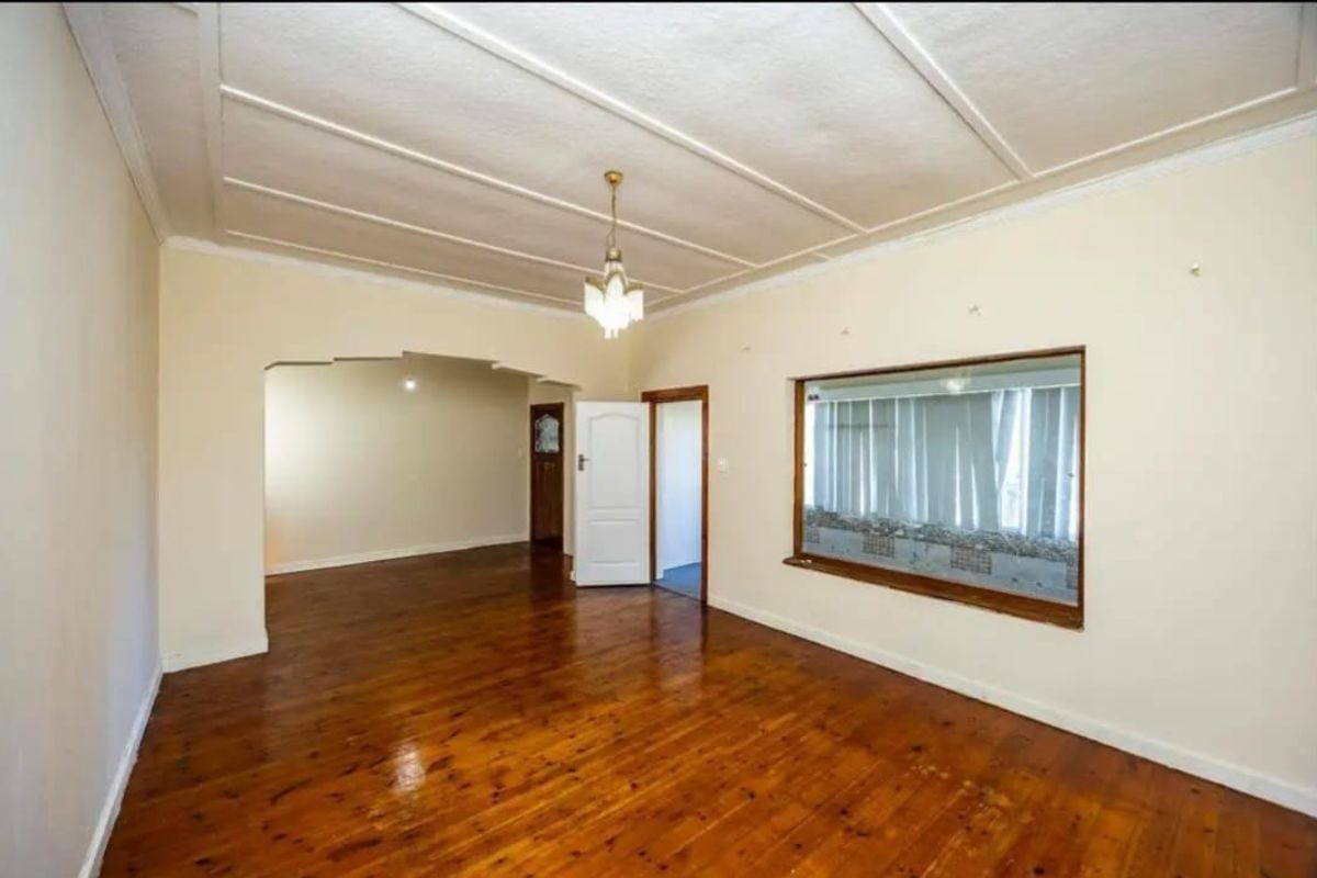 Spacious living room featuring original hardwood flooring, a decorative coffered ceiling, and a large picture window allowing for ample natural light.