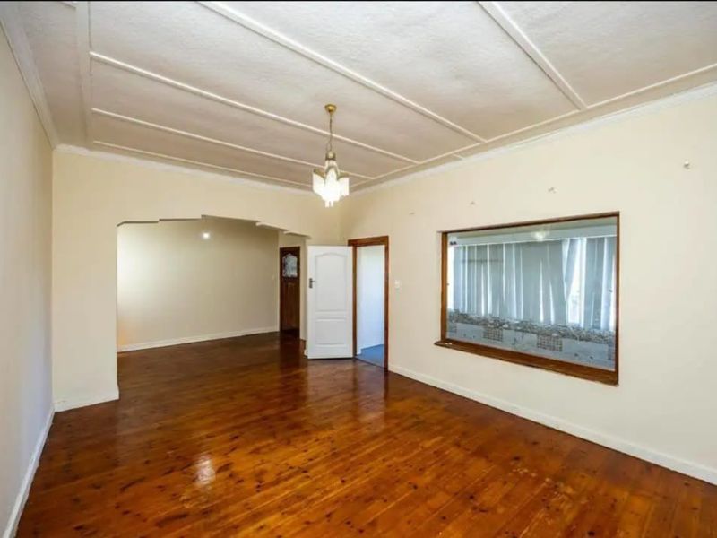 Spacious living room featuring original hardwood flooring, a decorative coffered ceiling, and a large picture window allowing for ample natural light.