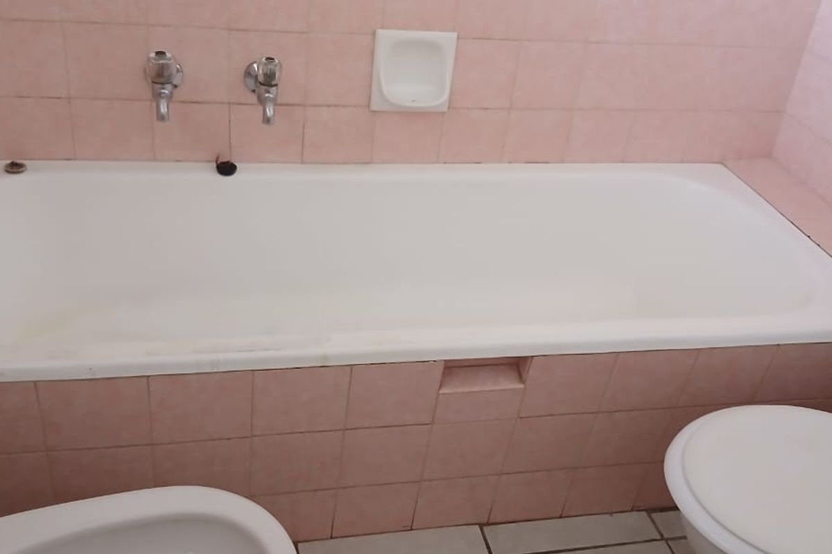 A dated bathroom featuring a built-in bathtub with wall-mounted taps, a toilet, and a bidet, finished with pink ceramic wall tiles.