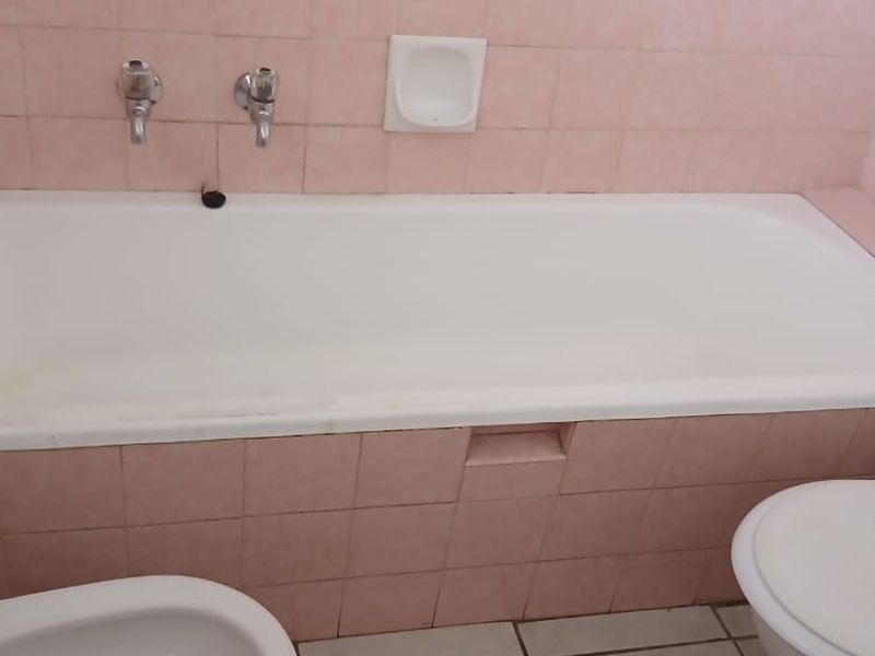 A dated bathroom featuring a built-in bathtub with wall-mounted taps, a toilet, and a bidet, finished with pink ceramic wall tiles.