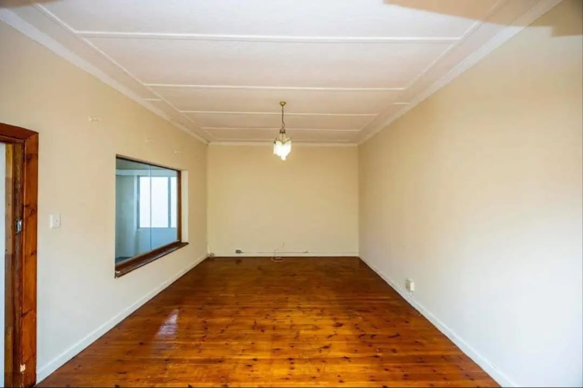 An empty living room featuring polished timber flooring, a ceiling rose, and an internal window looking into an adjacent space.