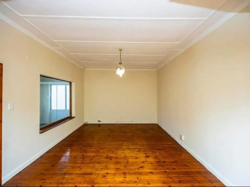 An empty living room featuring polished timber flooring, a ceiling rose, and an internal window looking into an adjacent space.