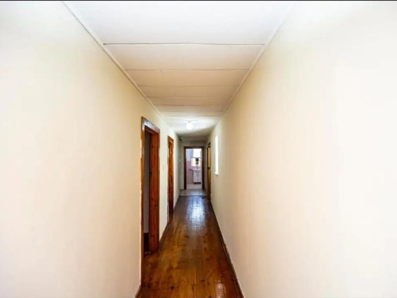 A long, empty hallway featuring polished hardwood flooring and timber door frames, providing access to various rooms within the apartment.