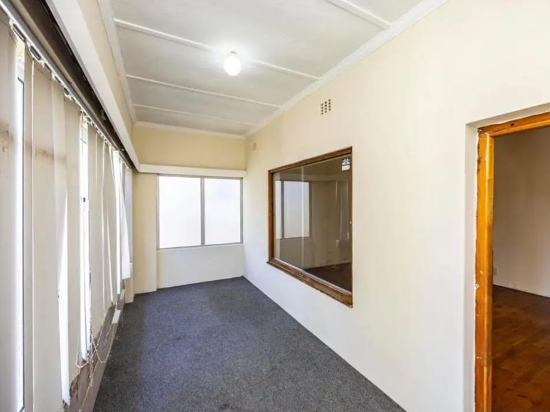 An empty, sunlit hallway featuring carpet flooring, vertical blinds, and an internal window looking into an adjacent room.