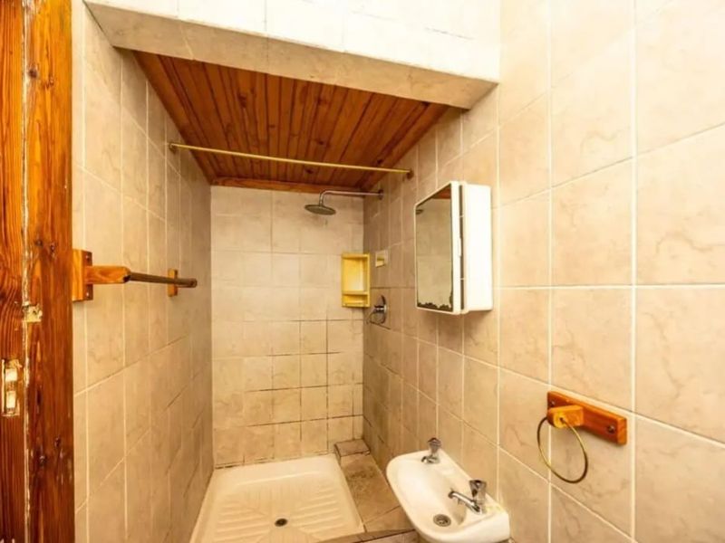 A compact bathroom featuring a shower enclosure with a timber ceiling, wall-mounted basin, and tiled walls, offering potential for a modern renovation.