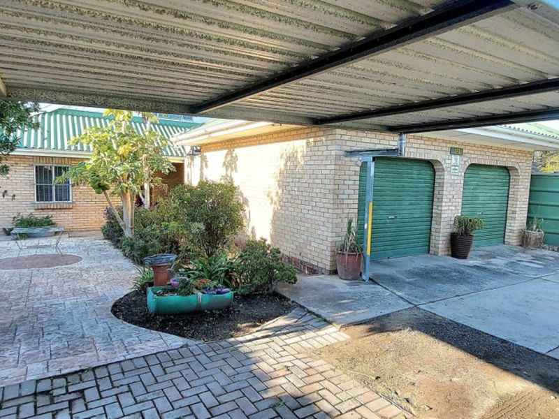 Front exterior view featuring a double garage, covered carport, paved driveway, and established garden area.