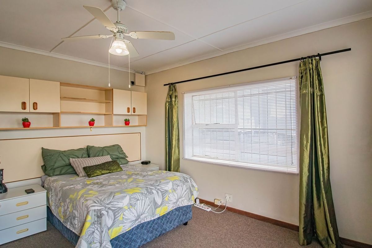 A bedroom featuring built-in cabinetry, a ceiling fan, carpeted flooring, and a large window with venetian blinds.