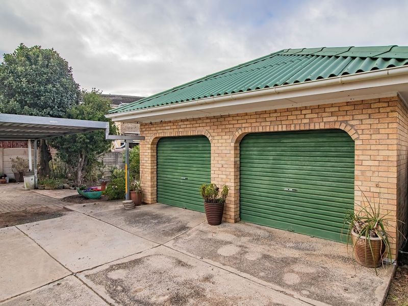 A double garage with green roller shutter doors, a matching corrugated roof, an adjacent carport, and a large water storage tank on the side.