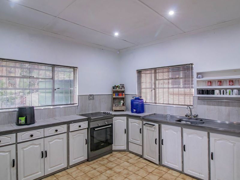 A functional kitchen featuring white cabinetry, stainless steel sink, freestanding oven, tiled splashbacks, and tiled flooring with ample natural light from dual windows.