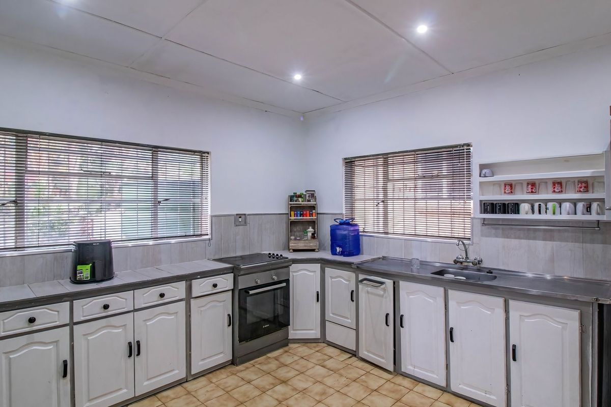 A functional kitchen featuring white cabinetry, stainless steel sink, freestanding oven, tiled splashbacks, and tiled flooring with ample natural light from dual windows.