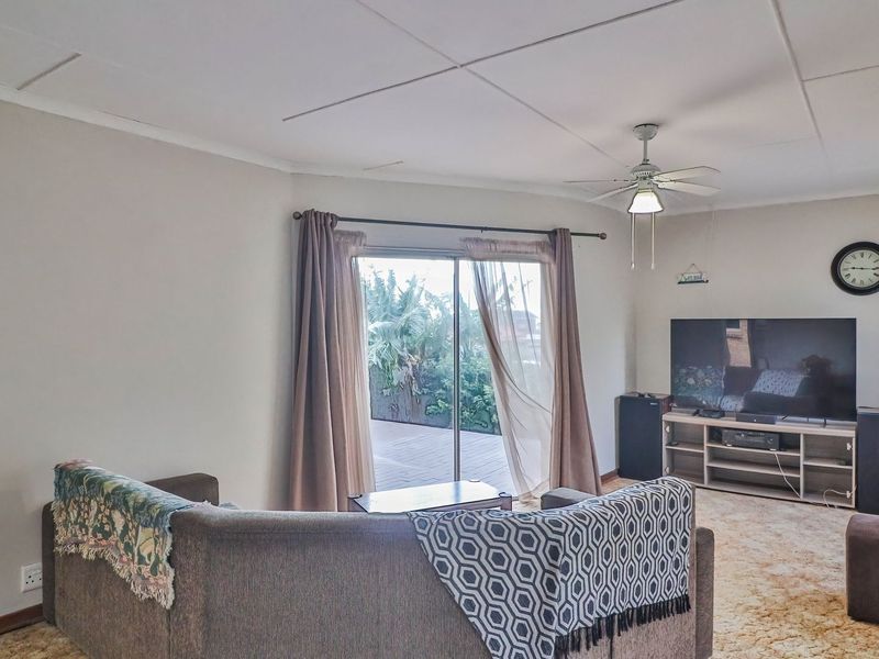 A living room featuring a ceiling fan, carpet flooring, and a sliding glass door providing access to the outdoor area.