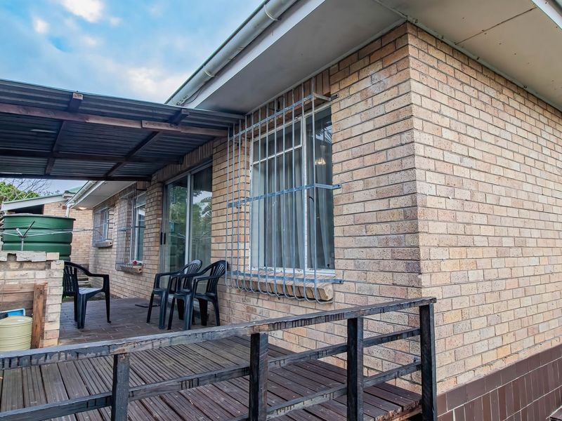 A covered outdoor patio area featuring brick exterior walls, timber decking, and security-barred windows, providing a functional space for outdoor living.