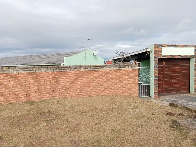 Front exterior view of the property featuring a brick boundary wall, a single garage with stone cladding accents, and a metal security gate.