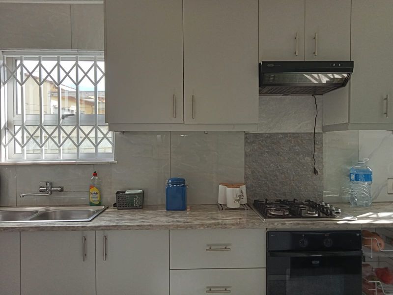A functional kitchen featuring light-toned cabinetry, a built-in oven with gas hob, extractor fan, and a stainless steel sink with a window security gate.